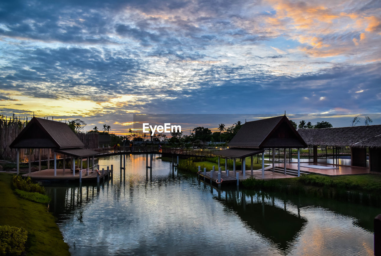 Houses by lake and buildings against sky during sunset