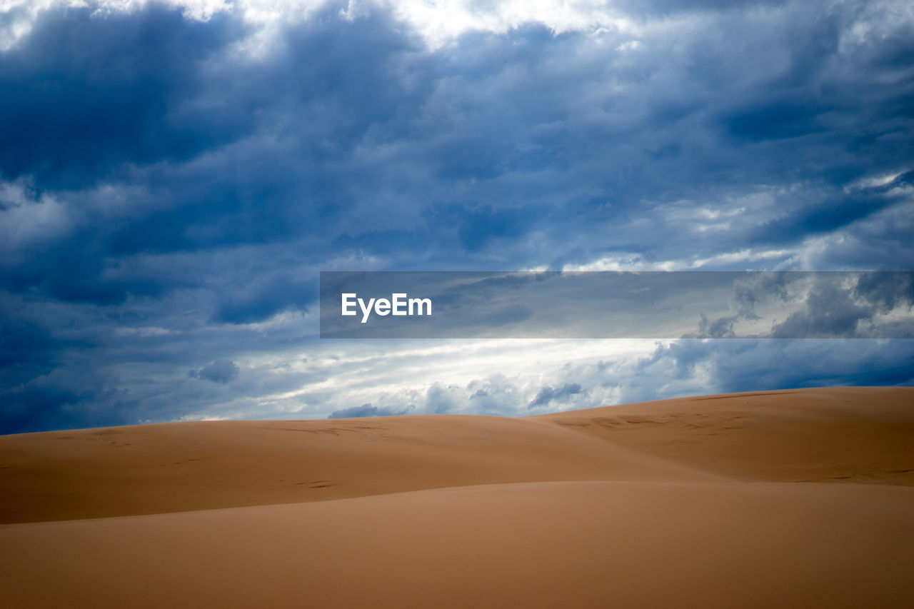 Sand dunes against cloudy sky at desert