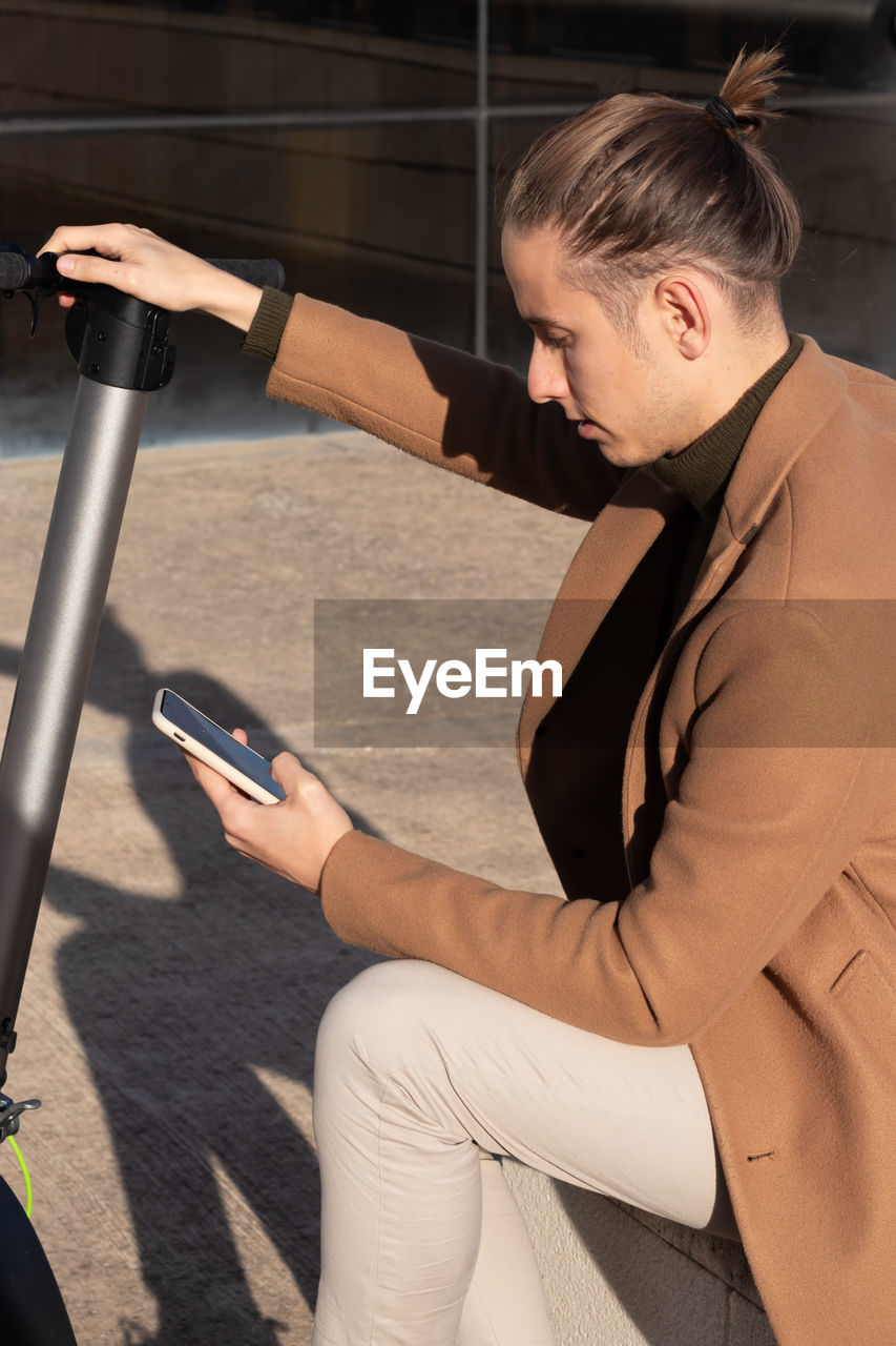 Young man sitting activating the electric scooter app on the smartphone to ride around city center