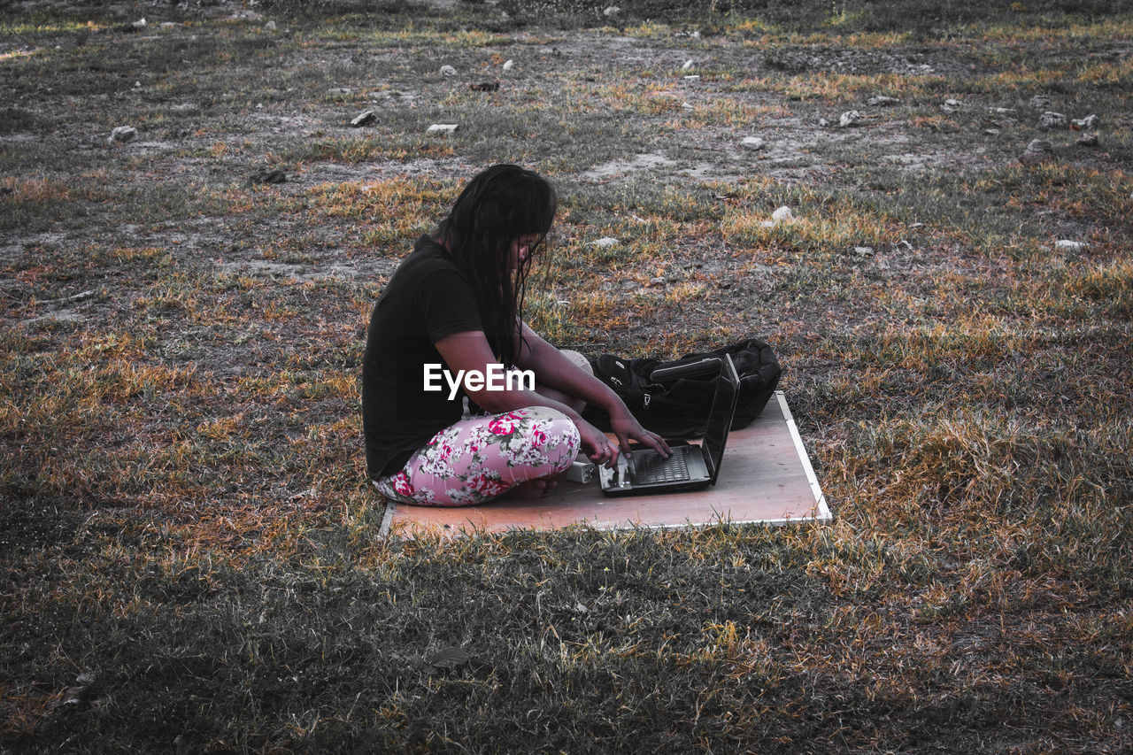 Side view of woman using laptop on field