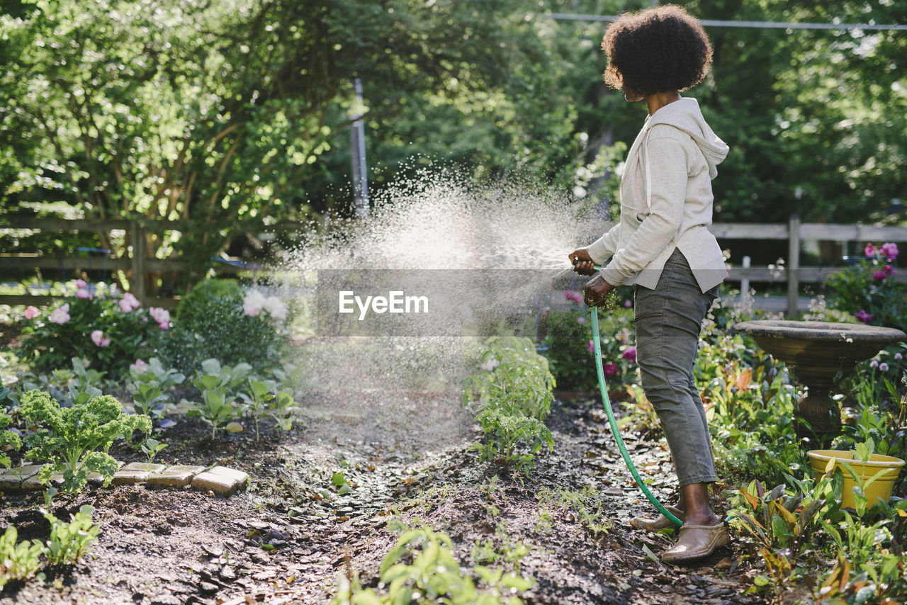 Side view of mature woman watering plants in yard