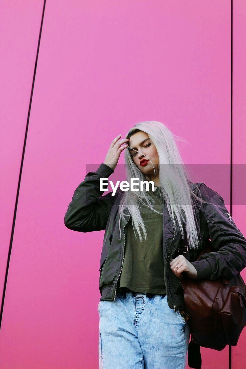 Young woman standing against pink wall