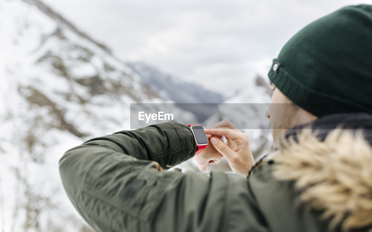 Spain, asturias, young man using smartwatch in the snowy mountains