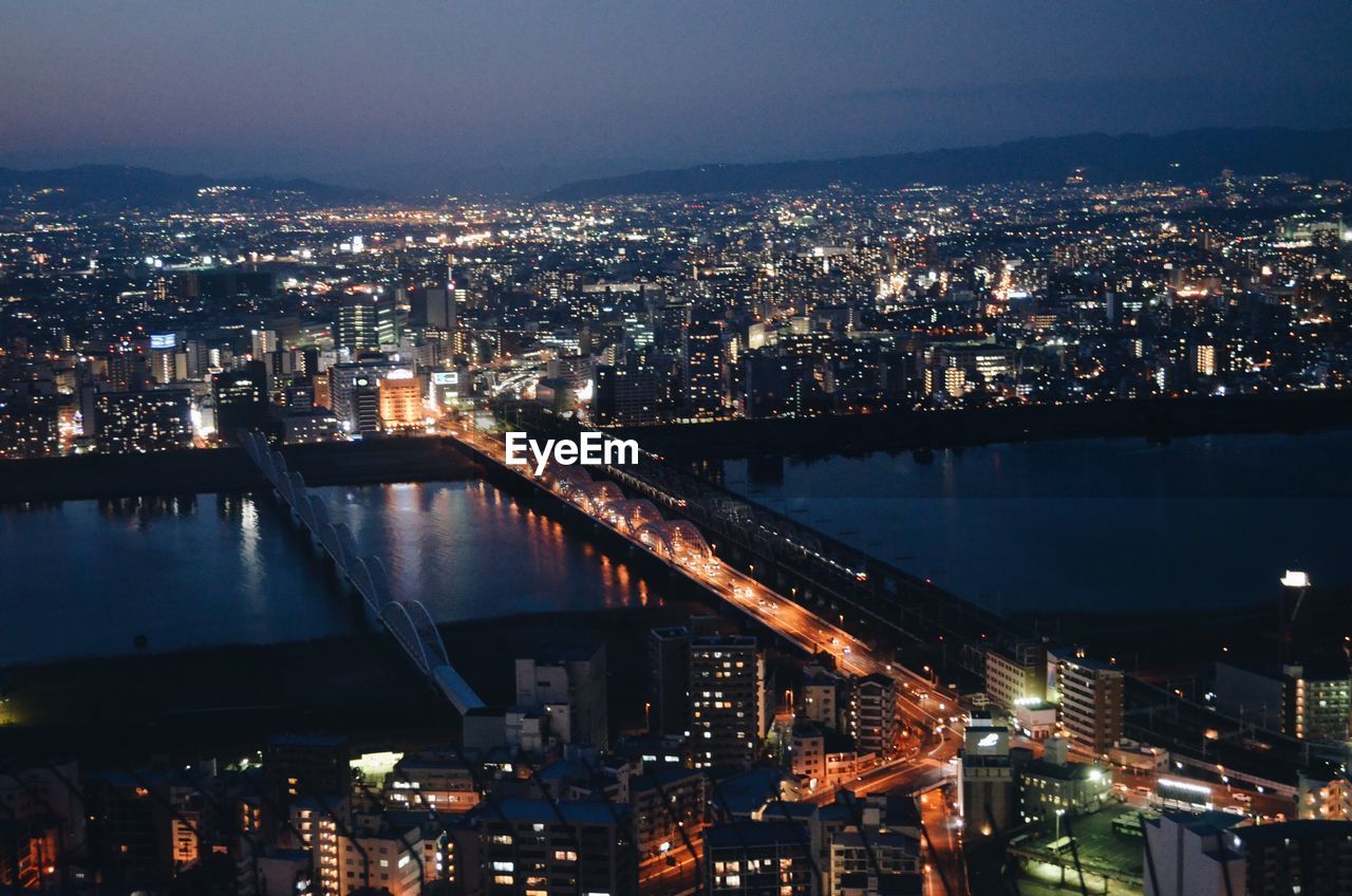 Illuminated cityscape by river against sky at night