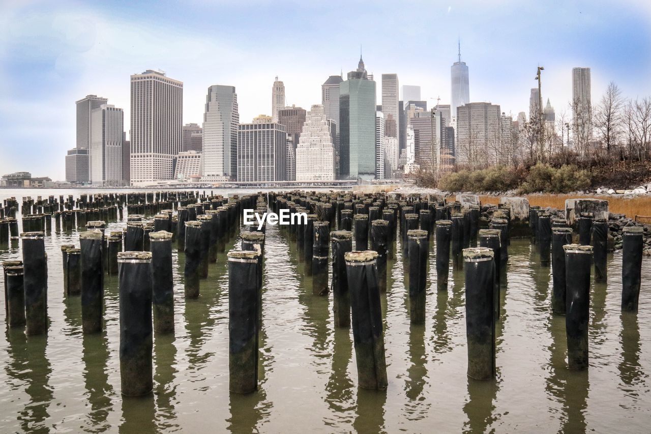 Wooden posts in east river against modern buildings at manhattan