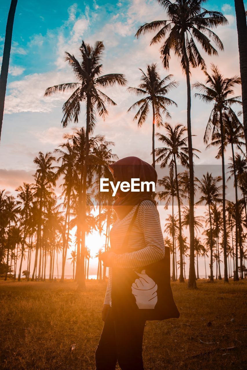 Woman standing on field against sky during sunset