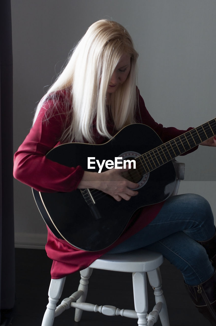 Beautiful young blonde woman in a red dress with a black guitar, favorite hobby