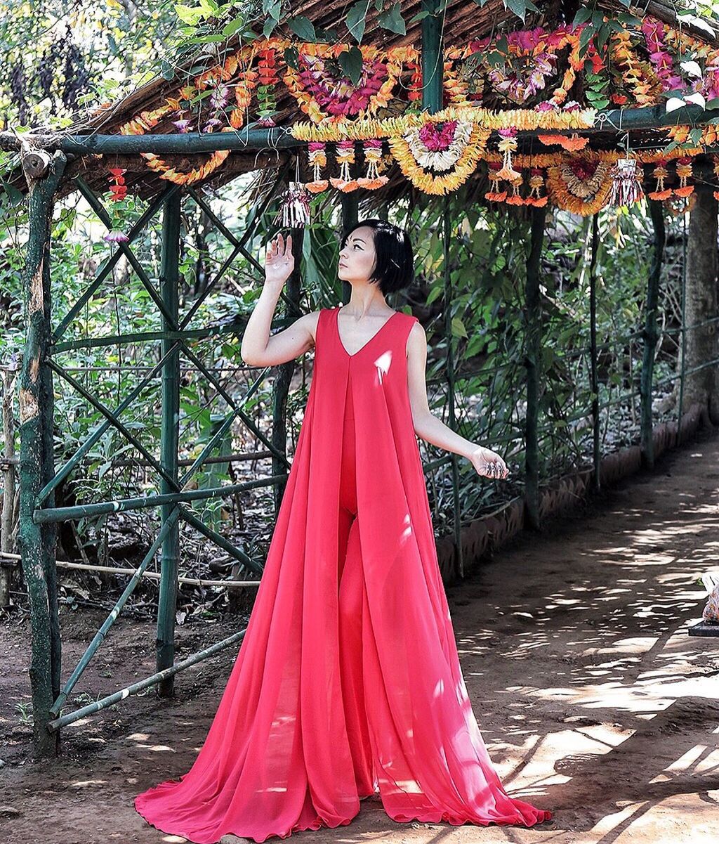 Woman wearing pink dress looking at floral garland while standing on covered walkway