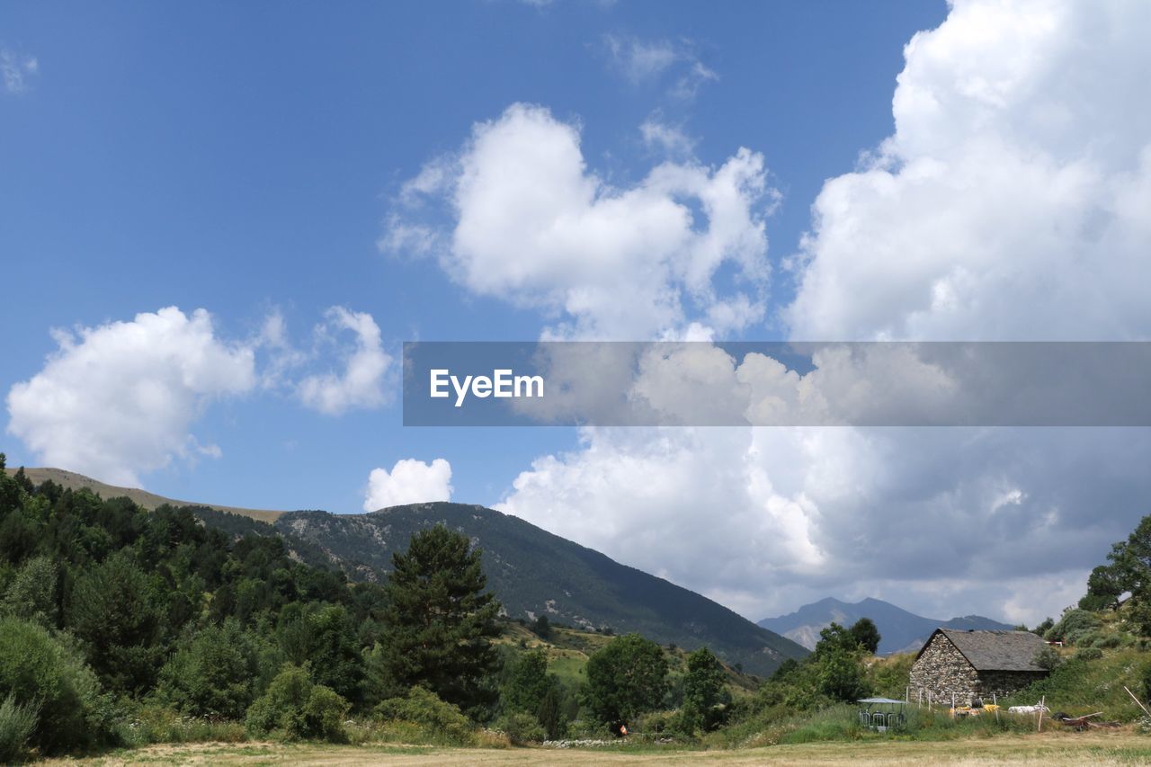 COUNTRYSIDE LANDSCAPE AGAINST MOUNTAINS AND CLOUDS