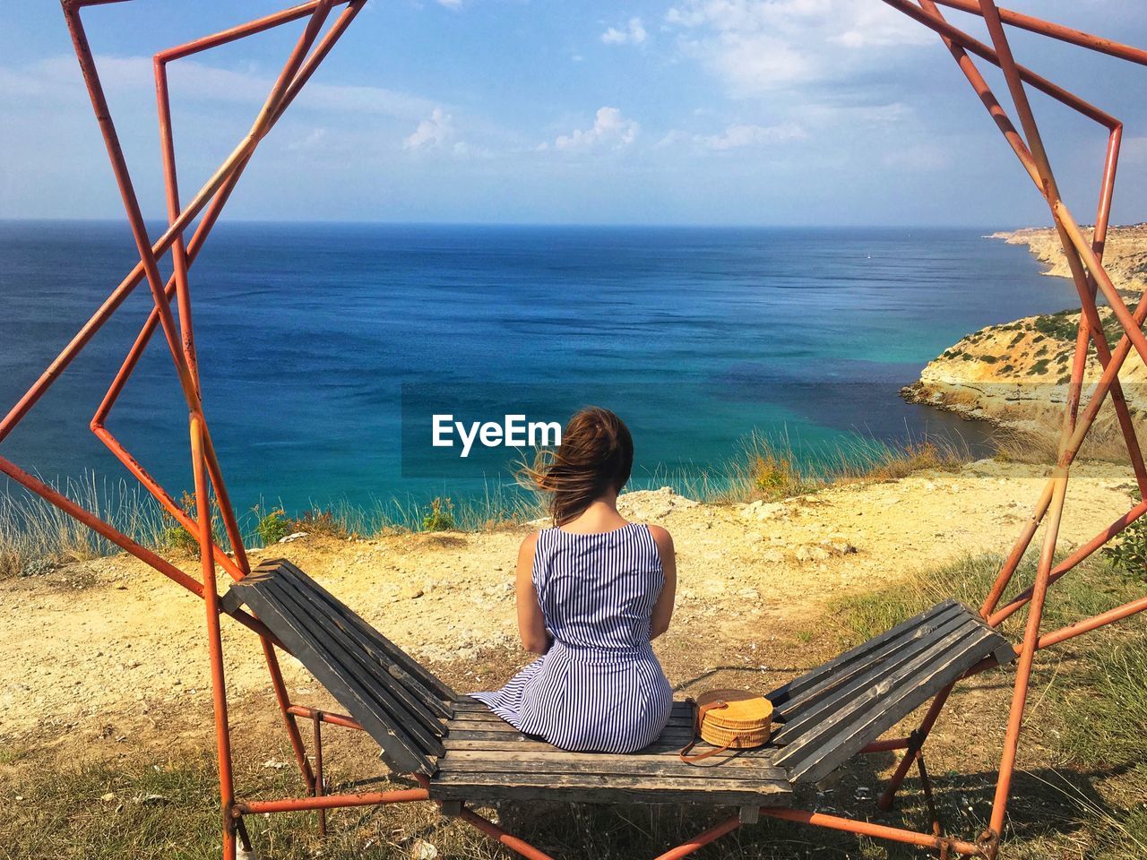 Rear view of woman sitting by sea against sky