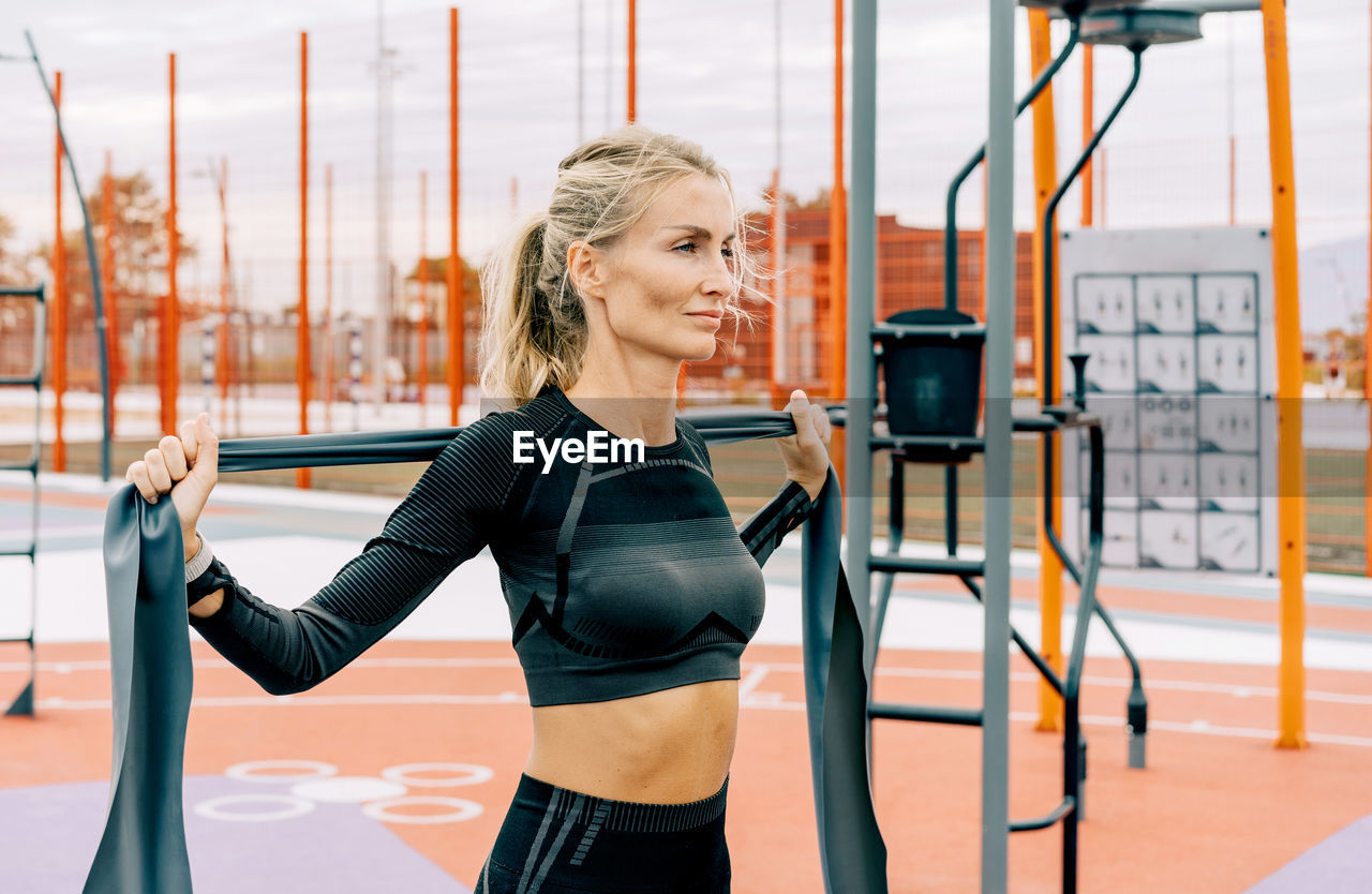 Young athletic woman is training on the sports ground using sports elastic bands.