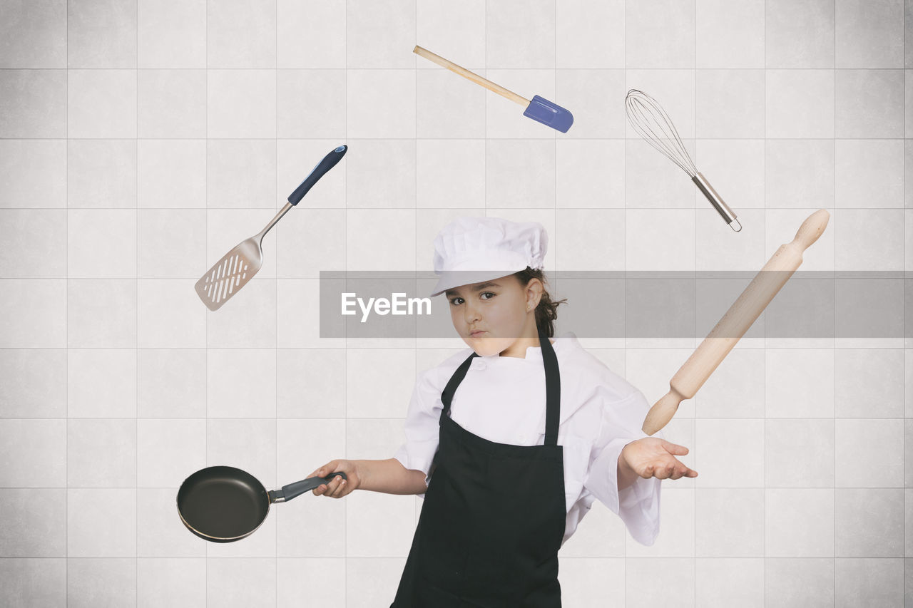 Portrait of girl wearing chef uniform juggling kitchen utensils