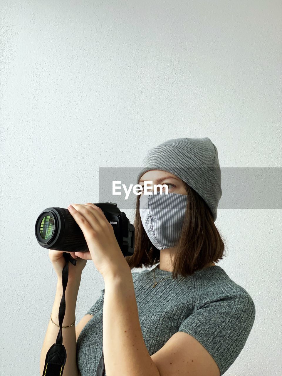 Young female photographer in reusable face mask with camera on a white background. photographing.