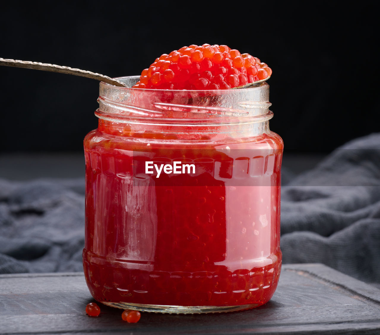 Fresh grainy red caviar in a glass jar on a wooden table