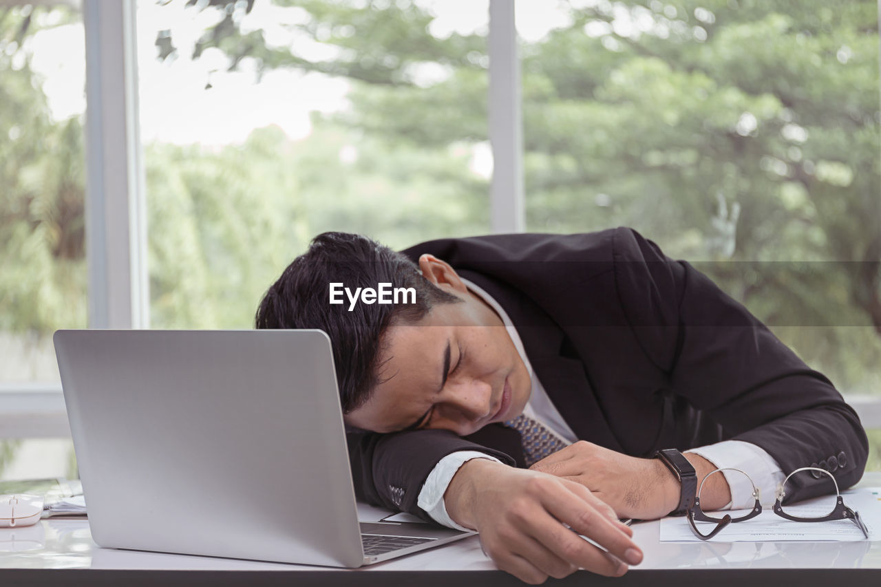 Businessman sleeping on desk against window in office