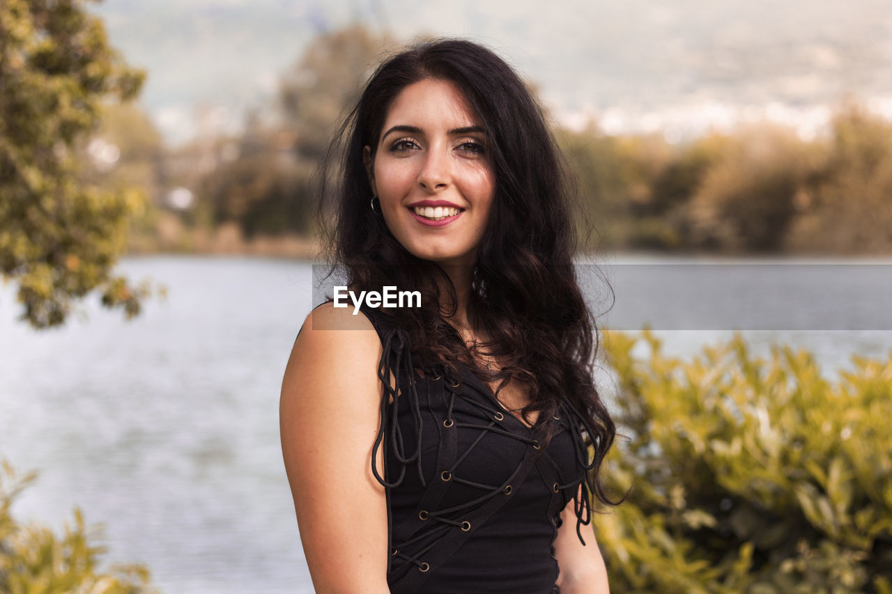 Portrait of smiling young woman standing against lake