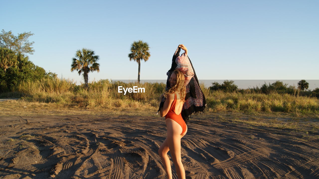 Portrait of young woman wearing one piece swimsuit holding scarf on sand