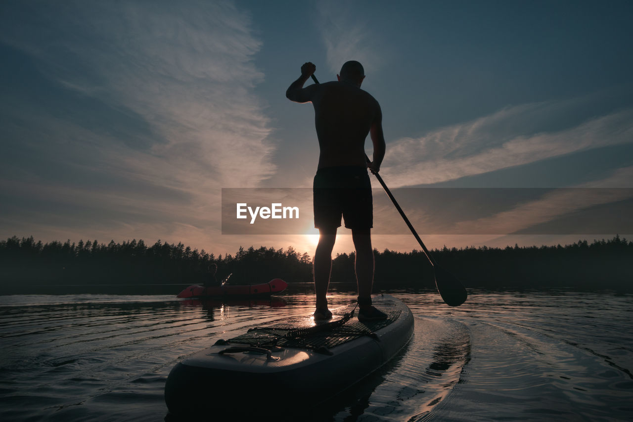 Silhouette of a sup surfer on a paddleboard in the backlight of the sunset sky. active  lifestyle