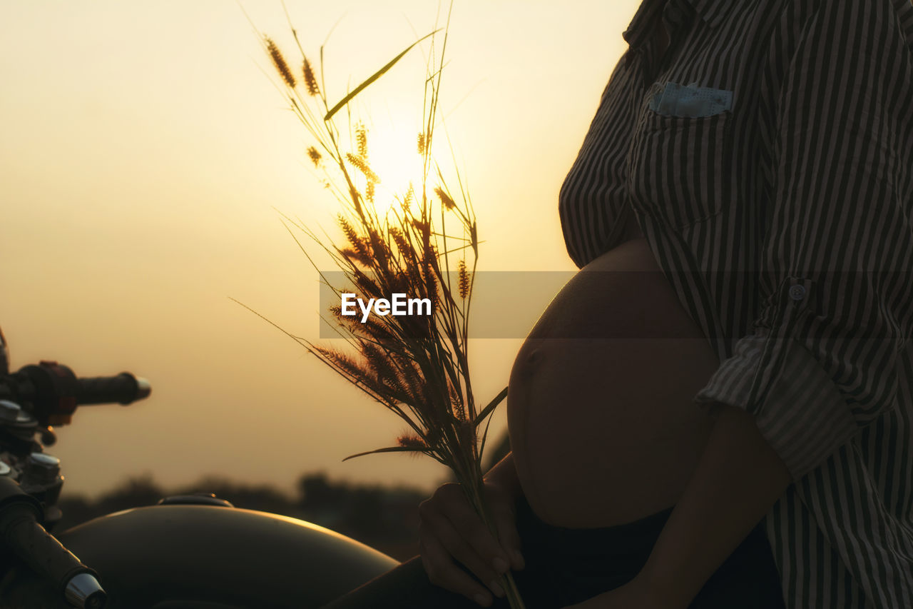 Midsection of pregnant woman against sky during sunset