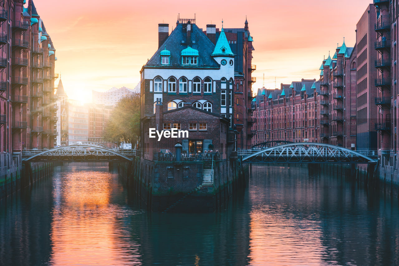 Canal amidst buildings in city during sunset