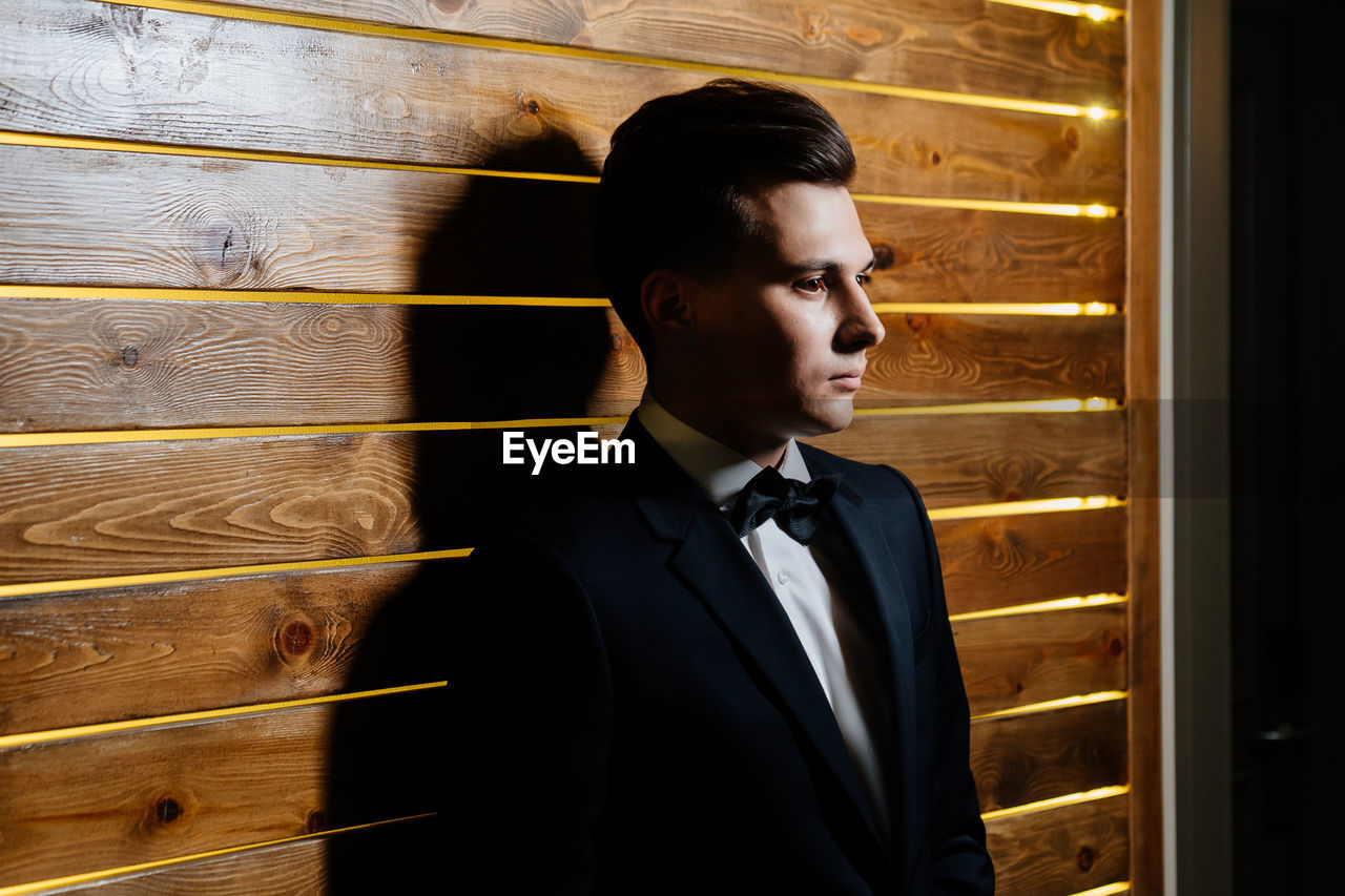 Young man looking away while standing against wall