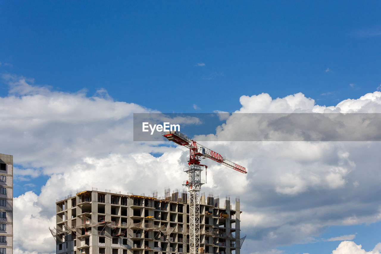 Building process of large residential apartment building with crane on cloudy sky background