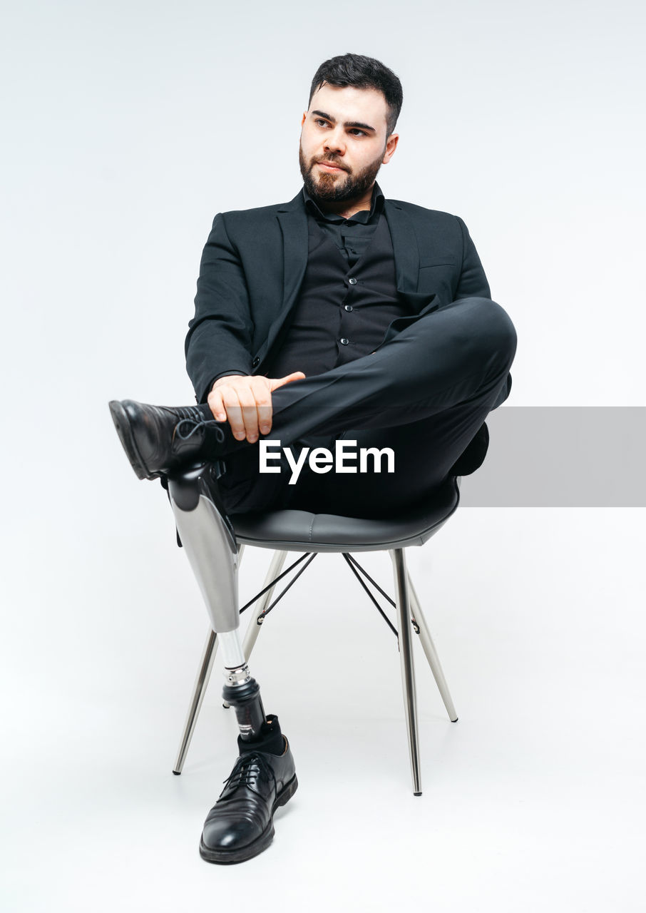 Young man sitting on chair against white background