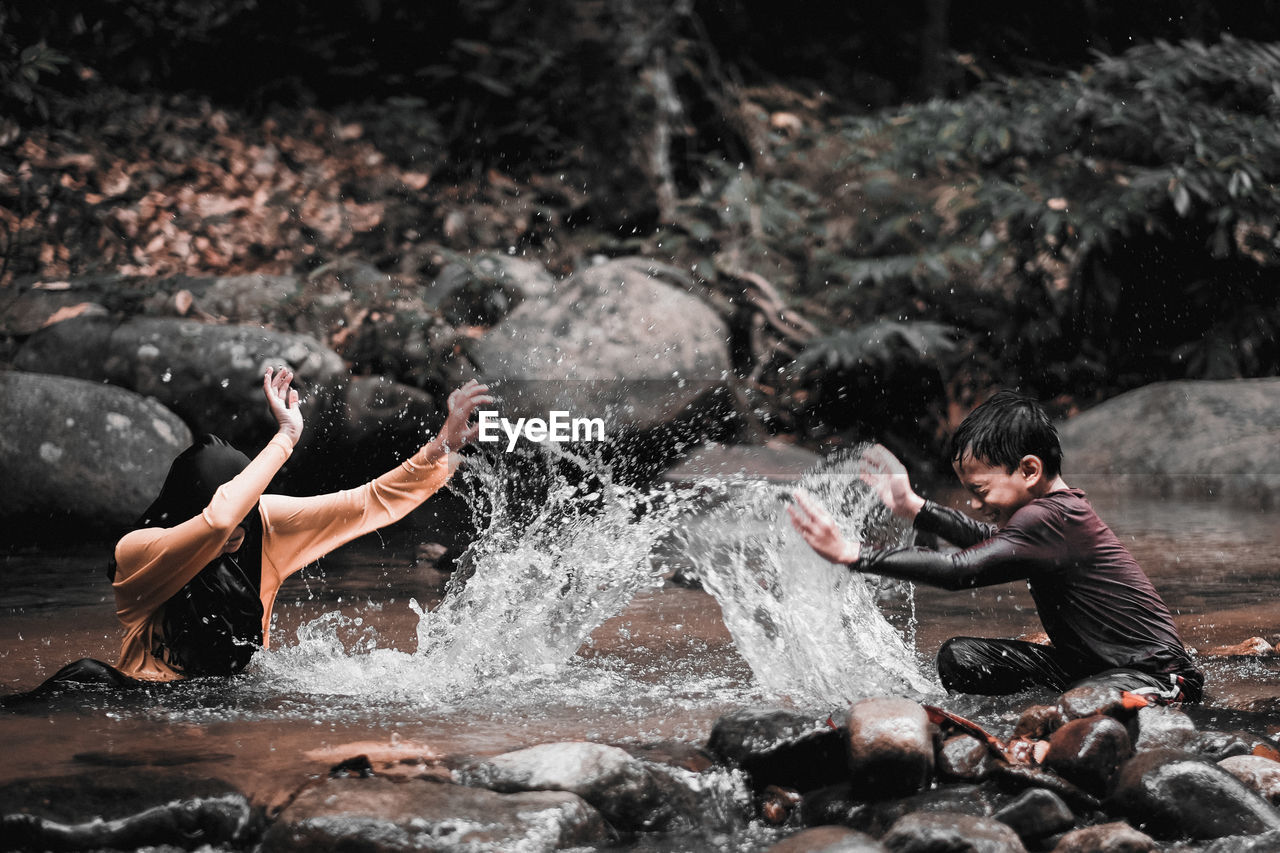 Cheerful siblings splashing water in river