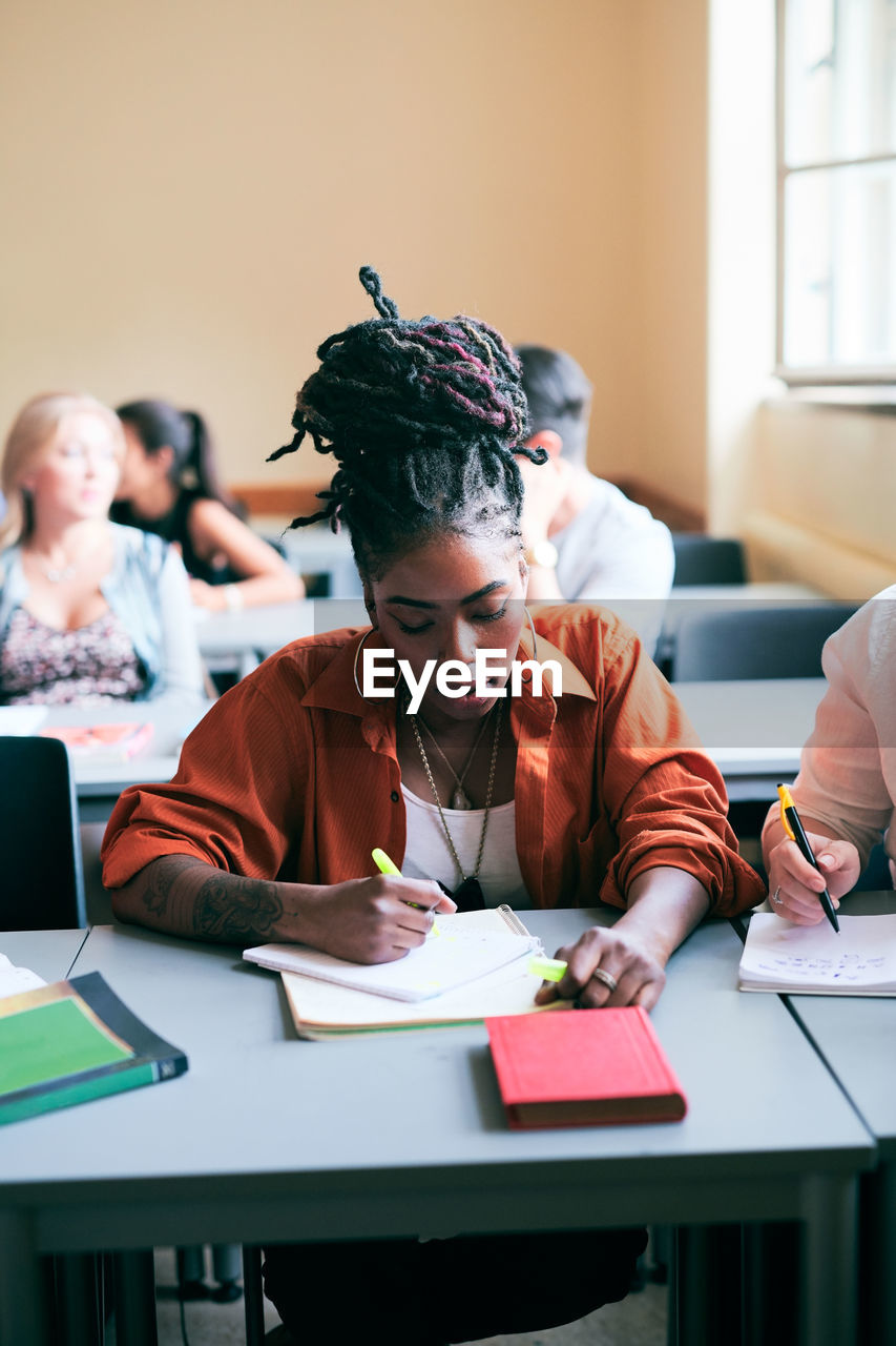 Confident young woman writing notes in classroom