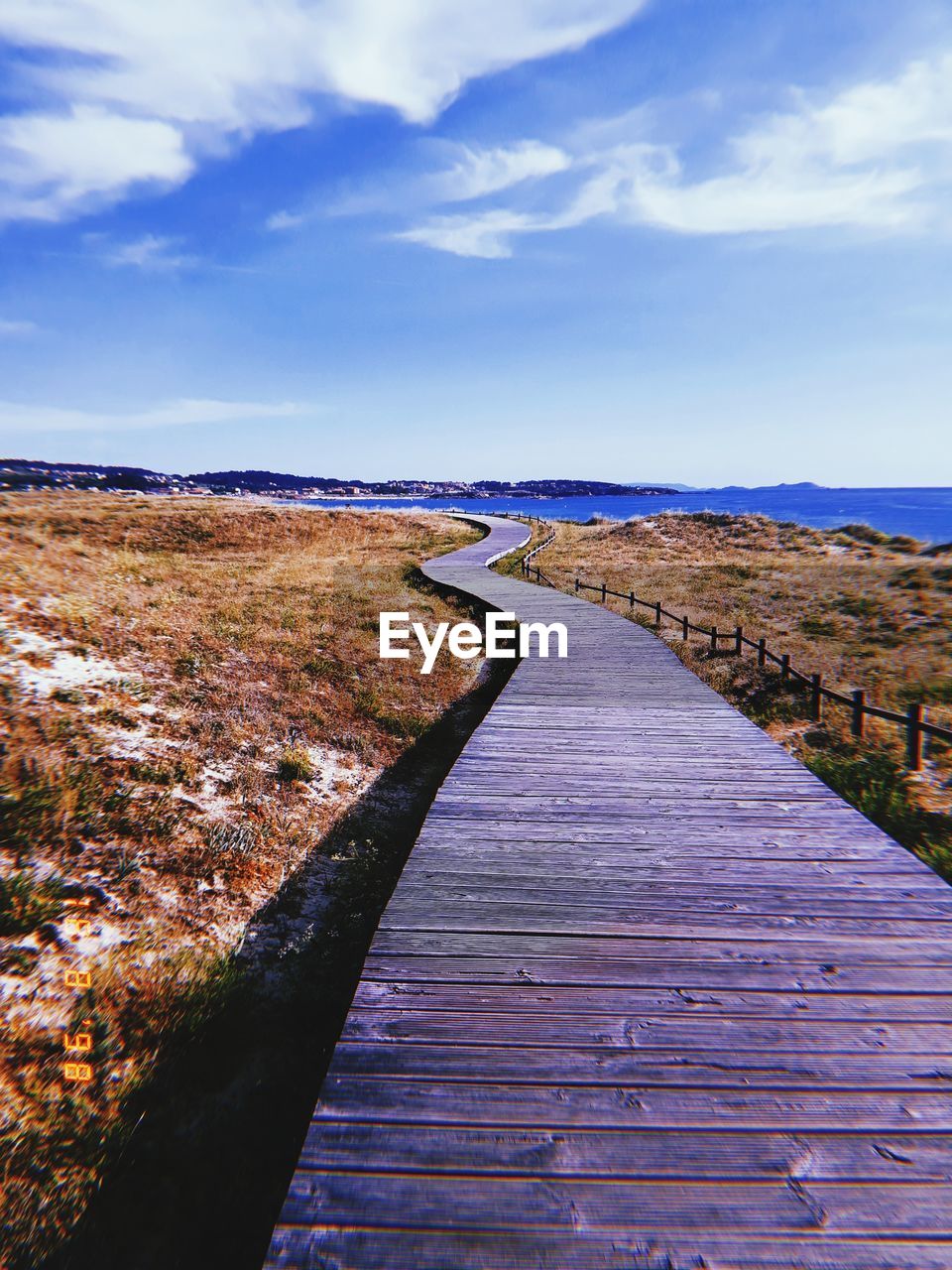 Boardwalk leading towards landscape against blue sky