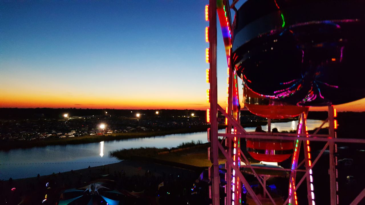 CLOSE-UP OF ILLUMINATED AMUSEMENT PARK AGAINST SKY AT SUNSET