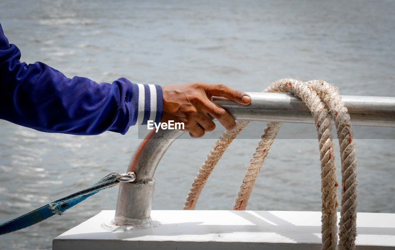 Cropped hand of man by rope against sea