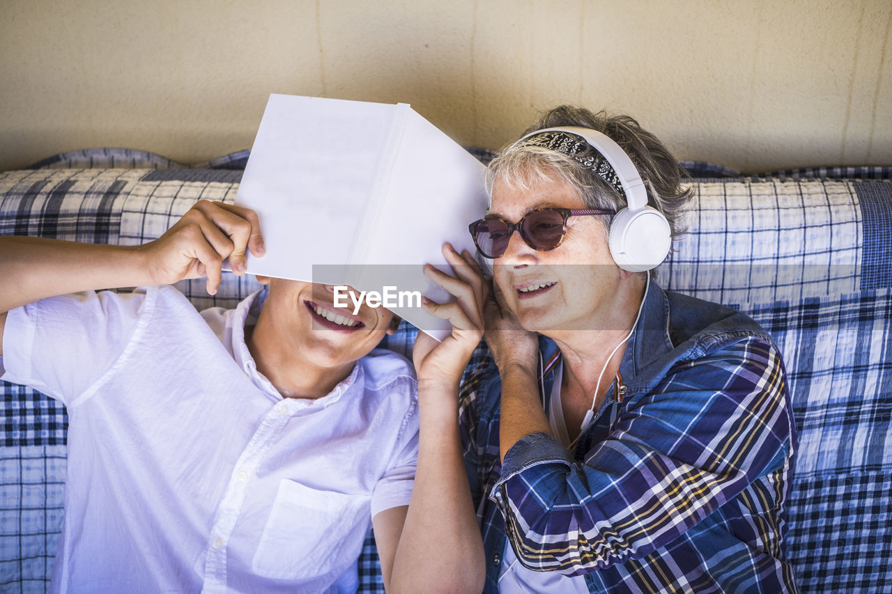 High angle view of grandmother wearing headphones while grandson covering face on bed at home