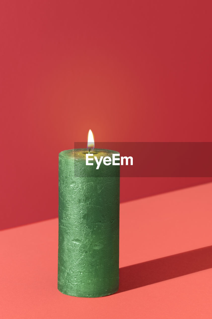 Christmas candle, burning, isolated on a red background. wax candle green colored. holiday  card.