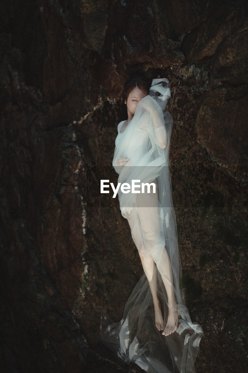 MIDSECTION OF WOMAN STANDING ON ROCK IN FOREST