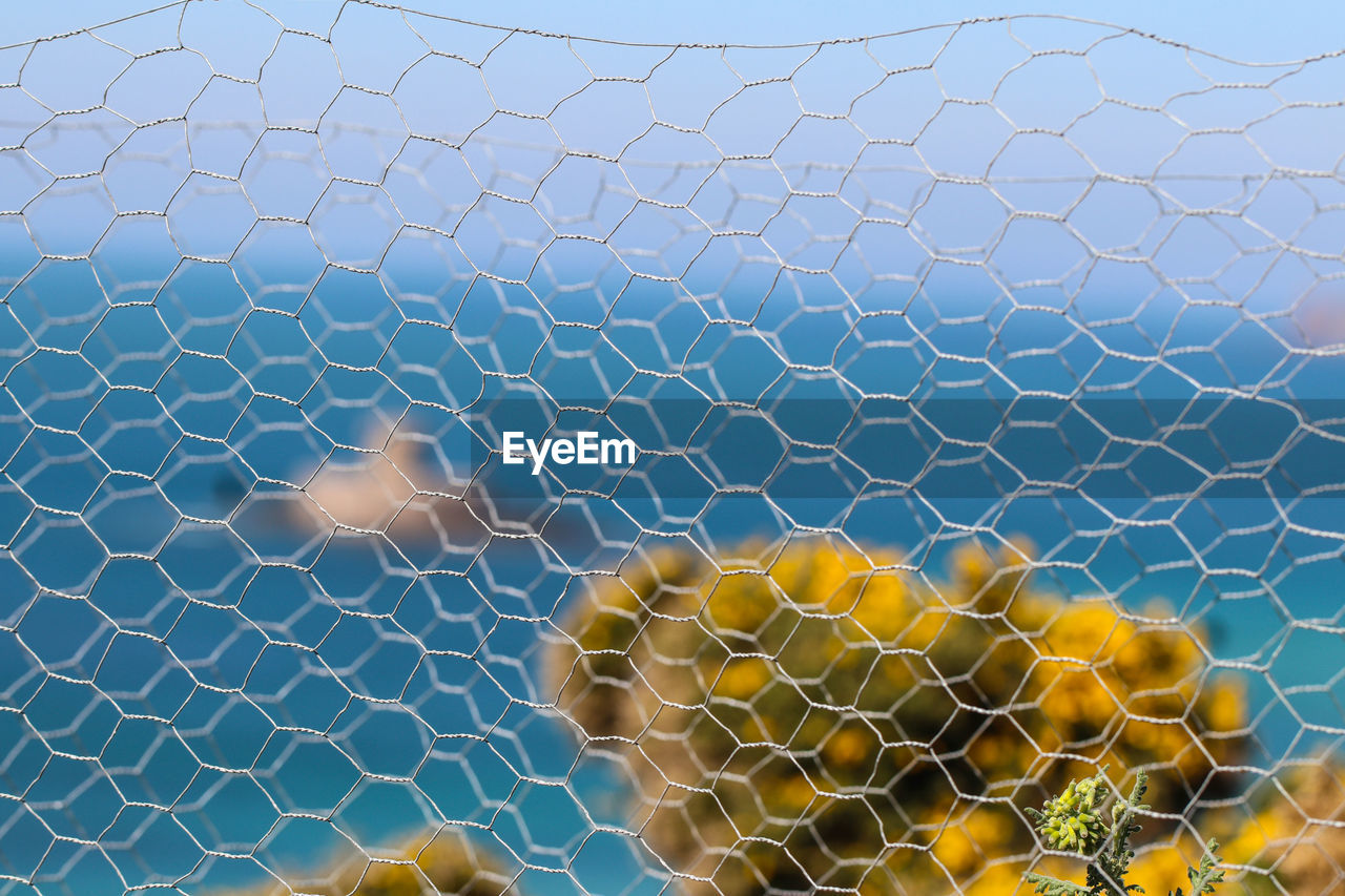 Close-up of chainlink fence against sea and sky