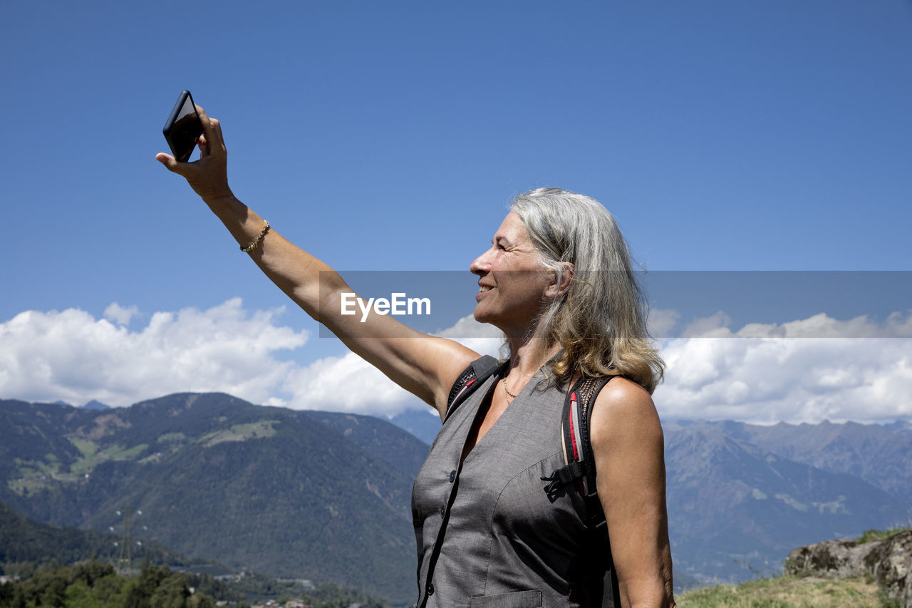 Smiling senior woman taking selfie through smart phone on sunny day