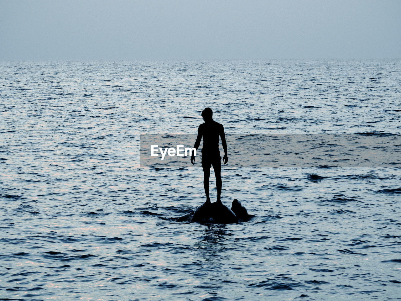 Silhouette man standing in sea against sky