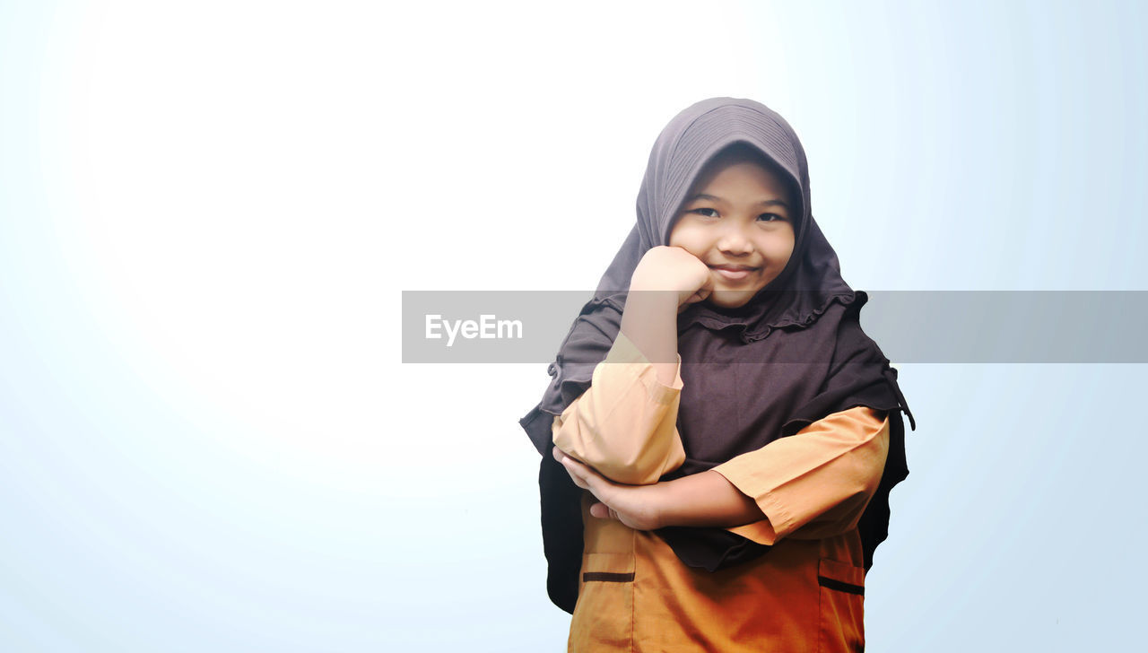 Portrait of happy girl wearing hijab while standing against clear sky