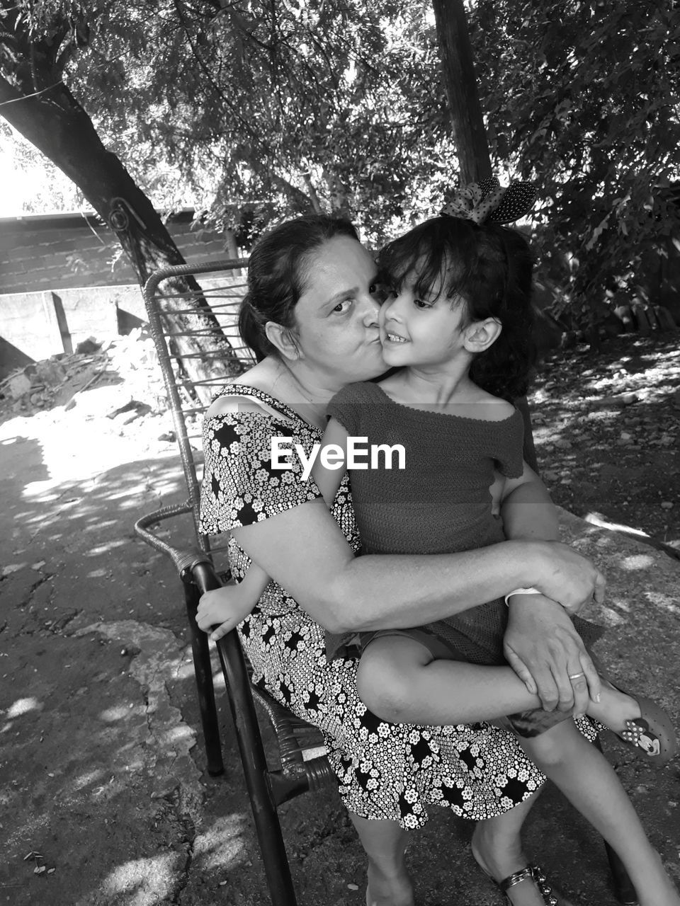 Portrait of mother kissing daughter while sitting on chair against trees