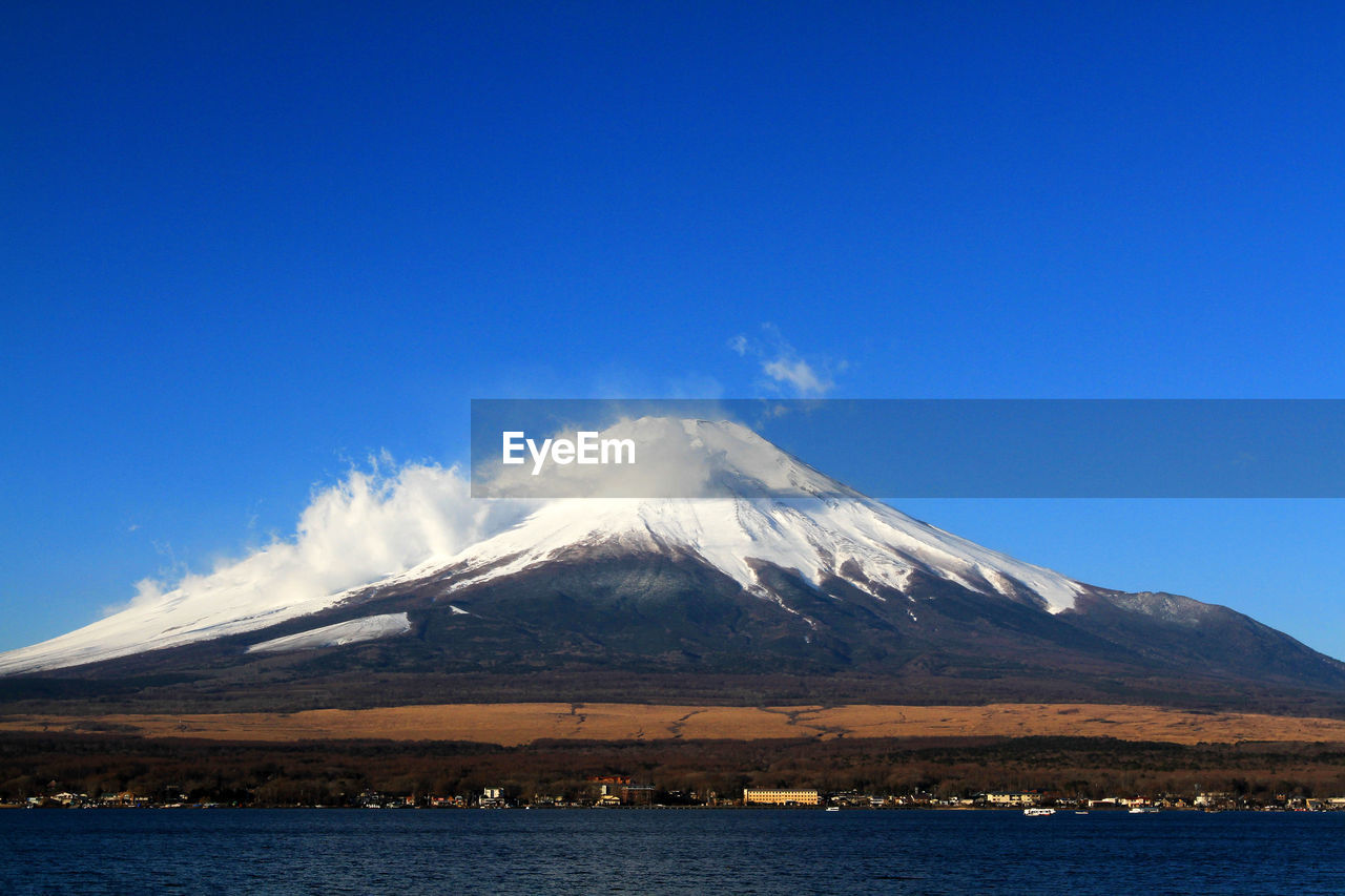 mountain, volcano, snow, sky, scenics - nature, stratovolcano, cold temperature, beauty in nature, landscape, winter, snowcapped mountain, water, environment, nature, travel destinations, horizon, blue, no people, land, sea, volcanic landscape, non-urban scene, travel, tranquil scene, geology, mountain peak, day, outdoors, tranquility, clear sky, tourism, cinder cone, cloud