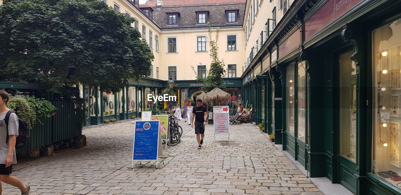 REAR VIEW OF WOMEN WALKING ON STREET AMIDST BUILDINGS