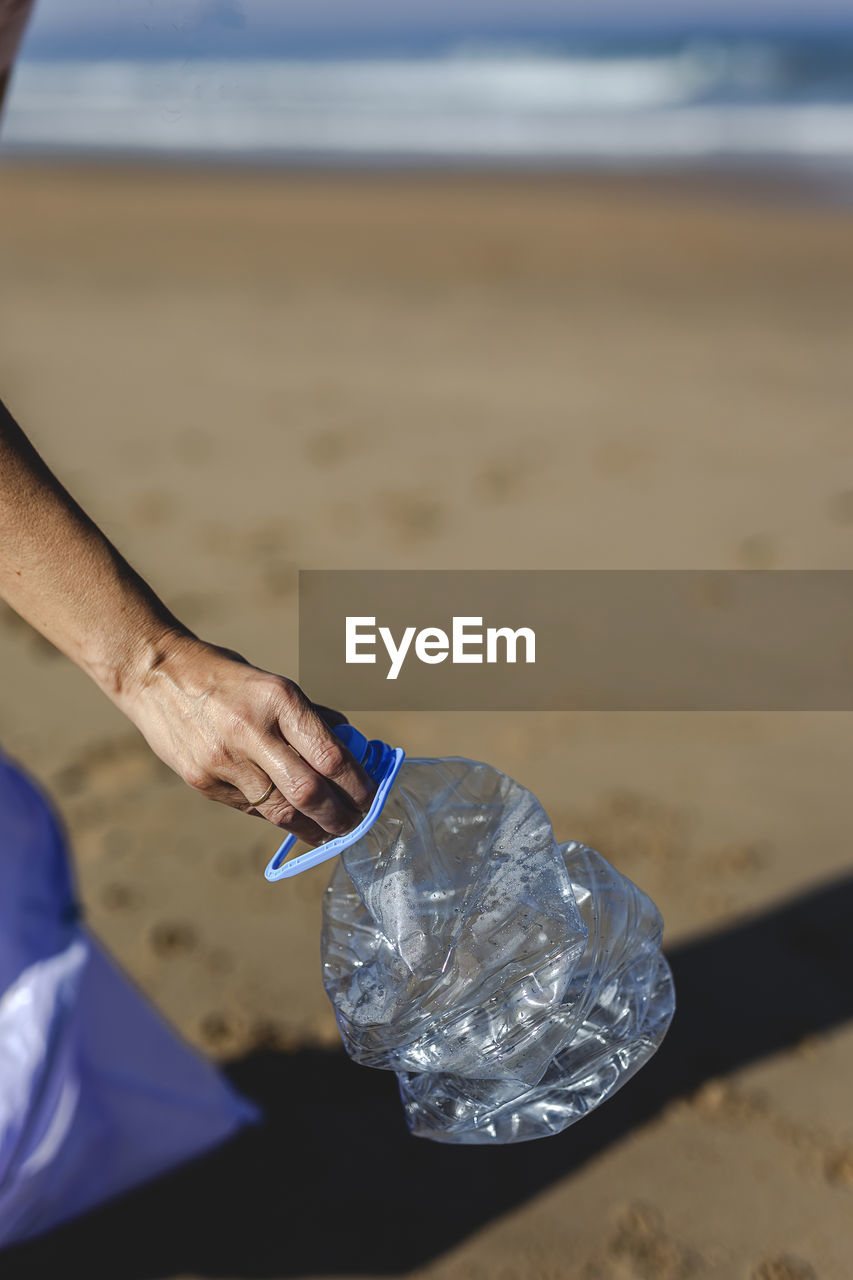 Cropped hand of person holding bottle at beach