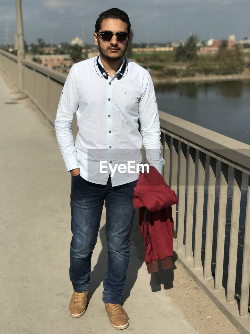 Portrait of young man wearing sunglasses while standing on bridge in city