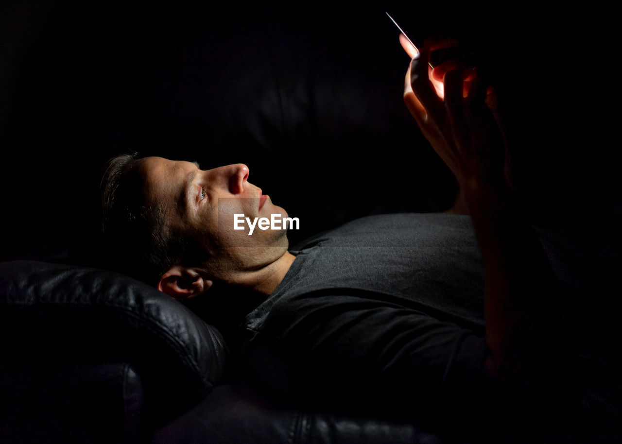Man using smart phone while lying on bed in darkroom