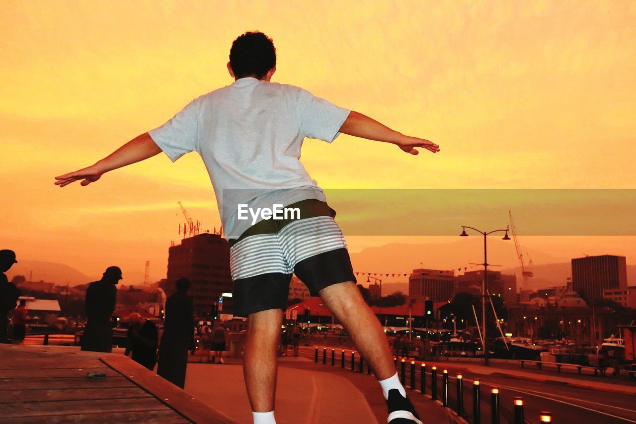 Rear view of teenager standing against orange sky