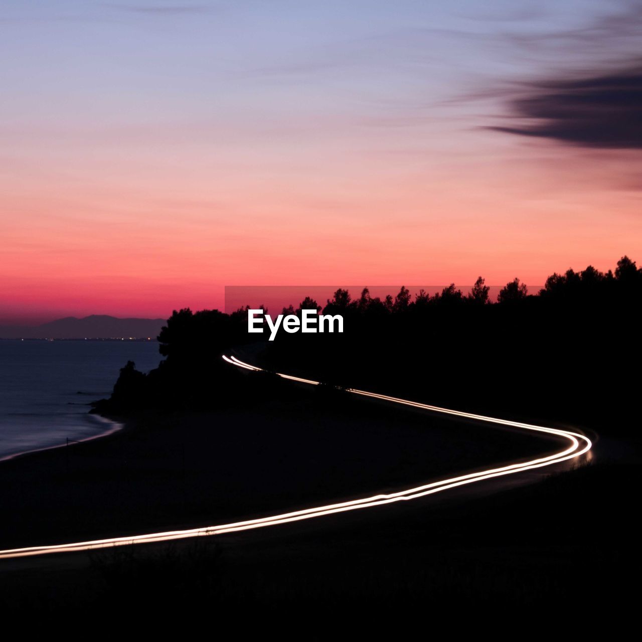 Silhouette trees by road against sky during sunset