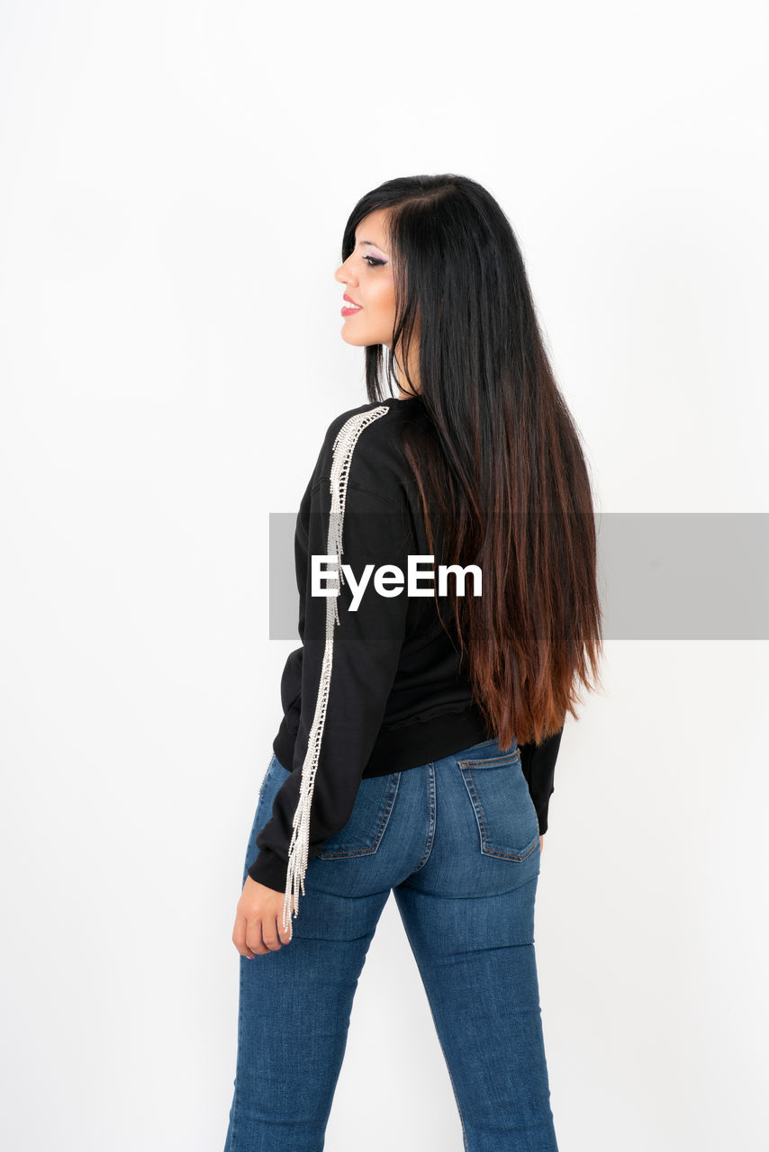 YOUNG WOMAN STANDING AGAINST WHITE BACKGROUND