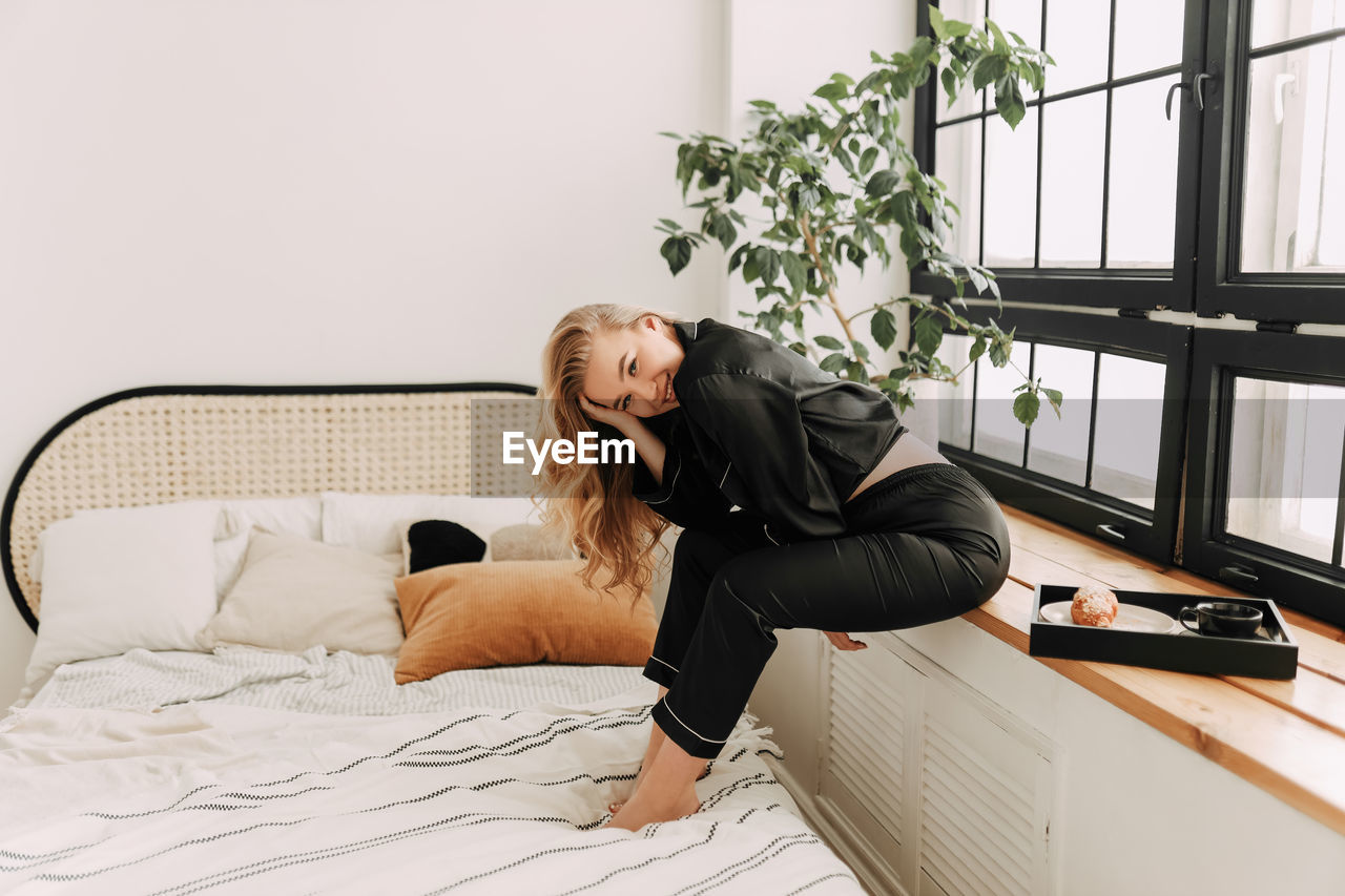 YOUNG WOMAN SITTING ON BED IN HOME