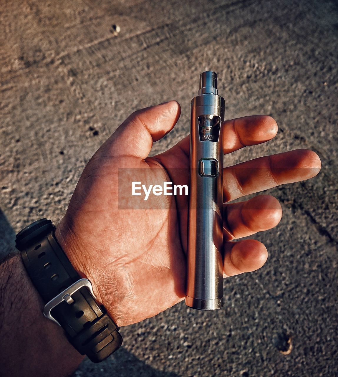 Cropped hand of man holding electronic cigarette on road